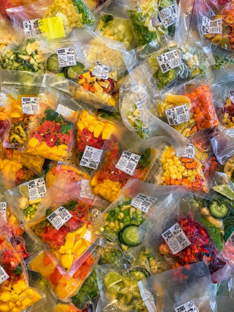 Naked Blends pre-packed fresh fruit and vegetable smoothie ingredient bags for weekly meal prep delivery in Playa del Carmen, showing colorful mango, dragon fruit, cucumber, spinach, and tropical produce packs